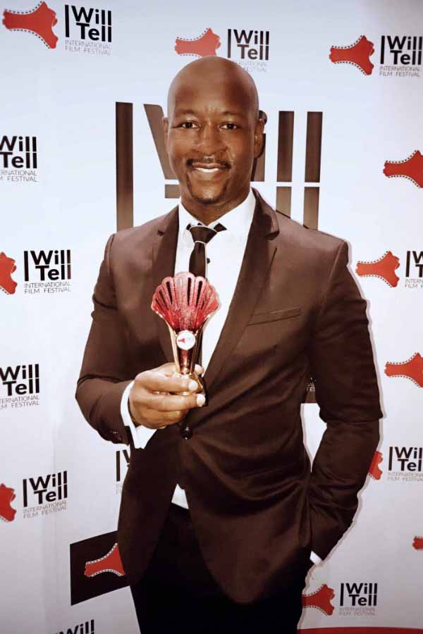 Home 67 International film festival awards winning filmmaker with his trophy against an I Will Tell backdrop.